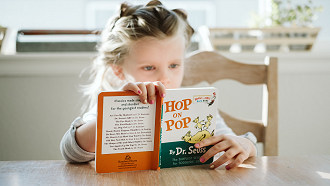 young girl reading Hop on Pop book while seated at table