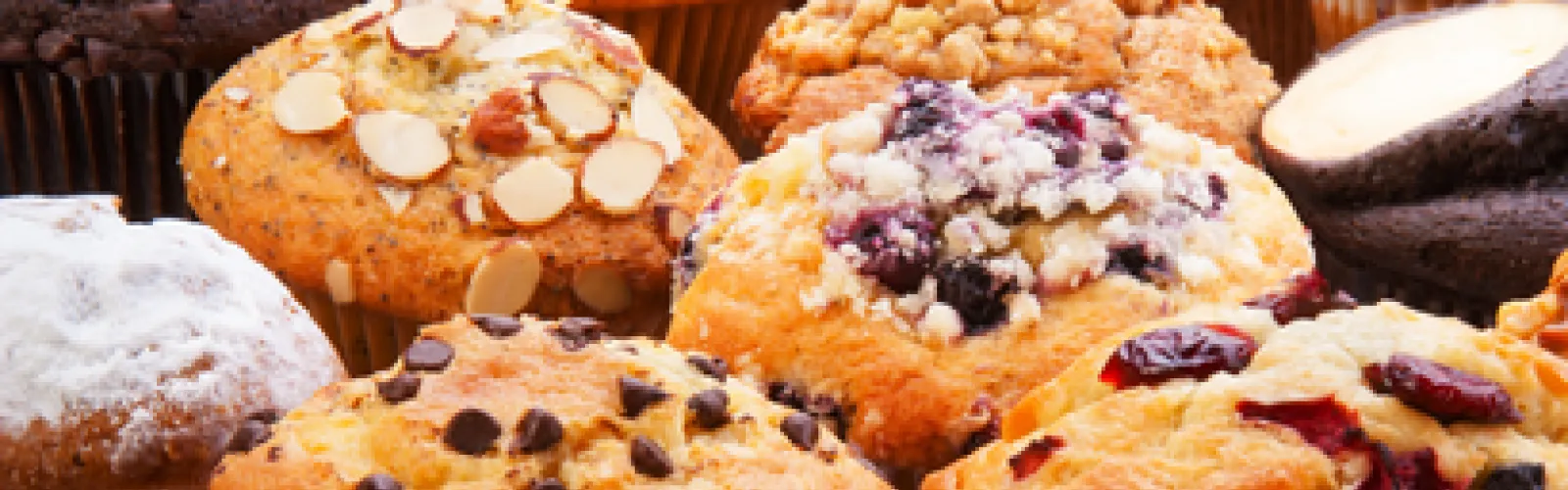 Many muffins with fruit, nuts and chocolate chips on top.